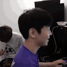 a young man in a purple shirt is typing on a computer keyboard