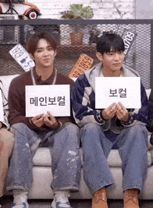 two young men sitting on a couch holding signs with korean writing