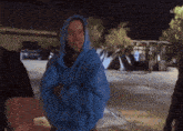a man wearing a blue hoodie stands in a parking lot at night