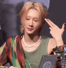 a young man wearing a pearl necklace and a colorful shirt is making a funny face .