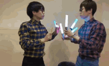 two young men in plaid shirts are holding light sticks
