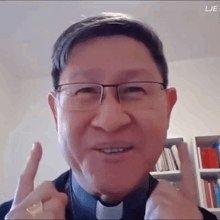 a man wearing glasses and a clergy collar is giving a thumbs up sign