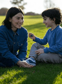 a woman and a boy are sitting in the grass playing with a toy