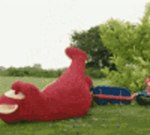 a red stuffed animal is laying on its back in a field .