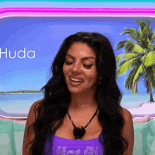a woman in a purple tank top is smiling in front of a palm tree and ocean .