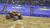 a monster truck is driving down a dirt track with a team hot wheels banner in the background