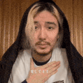 a man with long blonde hair and a beard is wearing a white shirt and a black hood