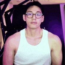 a man wearing glasses and a white tank top is standing in front of a purple wall