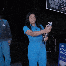 a woman in a blue jumpsuit holding a light saber in front of a sign that says the holo flow