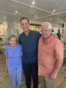 a man in a blue shirt poses with two older men