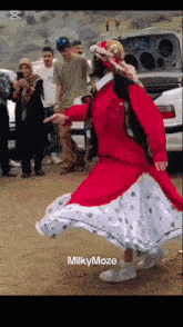 a woman in a red dress and white skirt is dancing in front of a crowd and the words milky maze are on the bottom