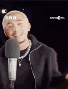 a man is singing into a microphone and smiling while wearing a necklace .