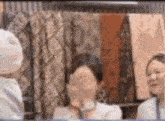 a group of people are sitting around a table and one of them is covering her face with her hands .