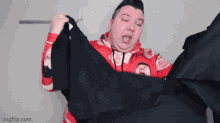a man in a red hoodie is holding a black shirt