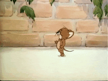 a cartoon mouse is standing in front of a brick wall with leaves hanging from it