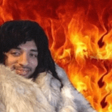 a man in a fur coat is smiling in front of a fire background .