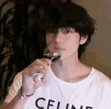 a young man wearing a celine t-shirt is drinking a glass of wine