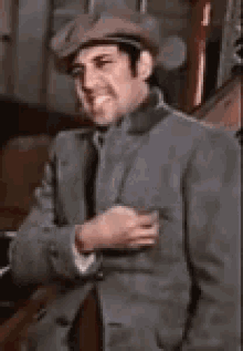 a man wearing a hat and a suit is smiling while holding his hand in his pocket .