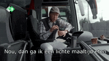a man sitting in the driver 's seat of a bus with the words nou dan ga ik een lichte maaltijd eten