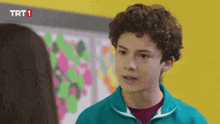 a boy with curly hair is talking to a girl in front of a wall that says trt1 on it