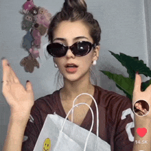 a woman wearing sunglasses and holding a white bag with a smiley face on it