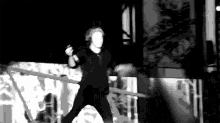 a black and white photo of a man standing on a stage holding a microphone .