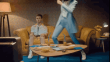 a man is sitting on a couch while a woman is dancing in front of him