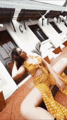 a woman in a yellow and white polka dot dress is sitting on the ground