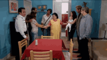 a group of people are standing around a table with a red tablecloth