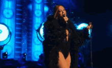 a woman in a fur coat singing into a microphone on a stage with a sign that says e on it