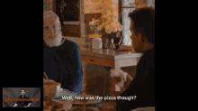 a man with a beard is sitting at a table talking to another man with the words well how was the pizza though