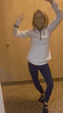 a woman wearing a white jacket and blue pants is dancing