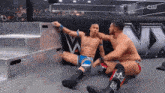 two wrestlers are sitting on the floor in front of a sign that says cw