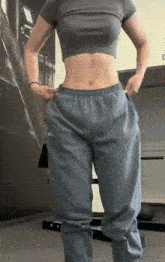 a woman wearing a grey crop top and blue sweatpants