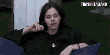 a woman in a black hoodie is sitting on a blue couch and making a face .