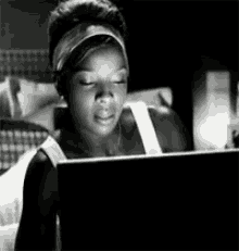 a black and white photo of a woman sitting in front of a laptop