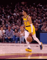 a basketball player wearing a yellow indiana jersey dribbles the ball