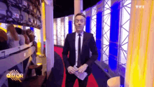 a man in a suit and tie stands on a red carpet in front of a tfi logo