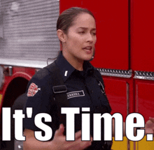 a woman in a firefighter uniform is standing in front of a red fire truck and says it 's time