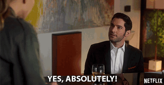 a man is sitting at a table with a glass of wine and says yes absolutely