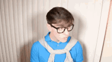 a young man wearing glasses and a blue polo shirt is standing in front of a white curtain .