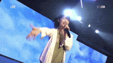 a woman is singing into a microphone on a stage in front of a screen that says live