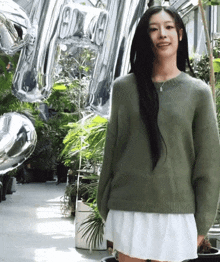 a woman wearing a green sweater and a white skirt stands in front of silver balloons that say ' aa '