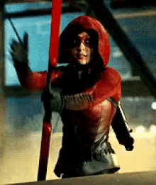 a woman in a red hooded costume is holding a red stick