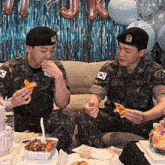 two soldiers are sitting on a couch eating pizza with balloons in the background