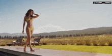 a woman in a bikini is standing in front of a field with mountains in the background and a banner that says pranay varma