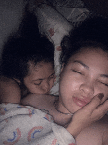 two girls are laying on a bed with one kissing the other on the cheek