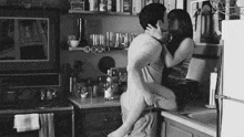 a man and a woman are kissing in a kitchen in a black and white photo .