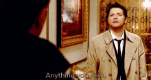 a man in a trench coat is talking to another man in a room .
