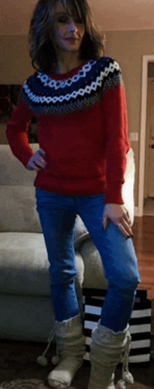 a woman in a red sweater and blue jeans is standing next to a couch